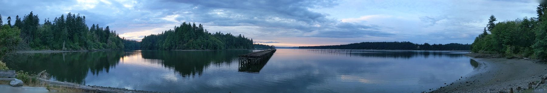Panoramic view from the Woodard Bay conservation area looking north over calm water toward the forested shores of Henderson Inlet and Chapman Bay